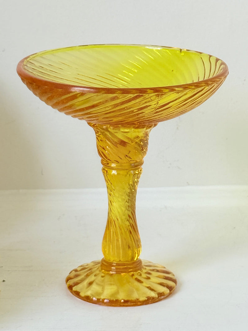 Amber pressed glass candle holder or compote with swirl design and pedestal base, photographed on a white background