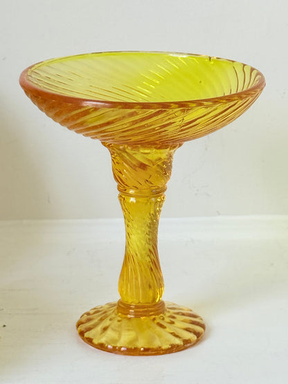 Amber pressed glass candle holder or compote with swirl design and pedestal base, photographed on a white background