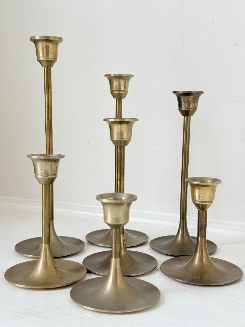 Set of 7 vintage brass candlesticks in graduated heights with aged brass finish styled with red ribbon on white surface