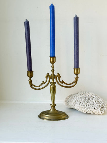 Vintage brass three-arm candelabra with curved arms and soft patina, photographed on a white surface