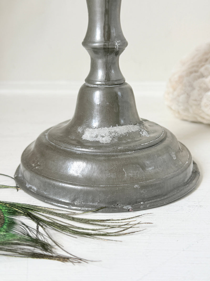 Antique pewter candlestick with baluster stem and aged patina styled with coral candle on white surface