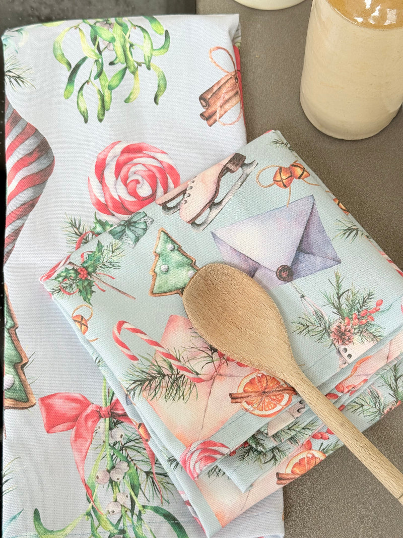 Pair of pastel blue festive tea towels with candy cane and ribbon print, folded, photographed on a kitchen worktop