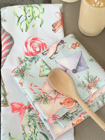 Pair of pastel blue festive tea towels with candy cane and ribbon print, folded, photographed on a kitchen worktop