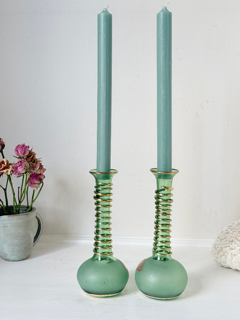 Pair of vintage green glass candlesticks with gold detail and spiral stems styled with blue taper candles on white surface