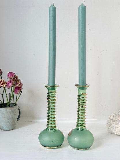 Pair of vintage green glass candlesticks with gold detail and spiral stems styled with blue taper candles on white surface