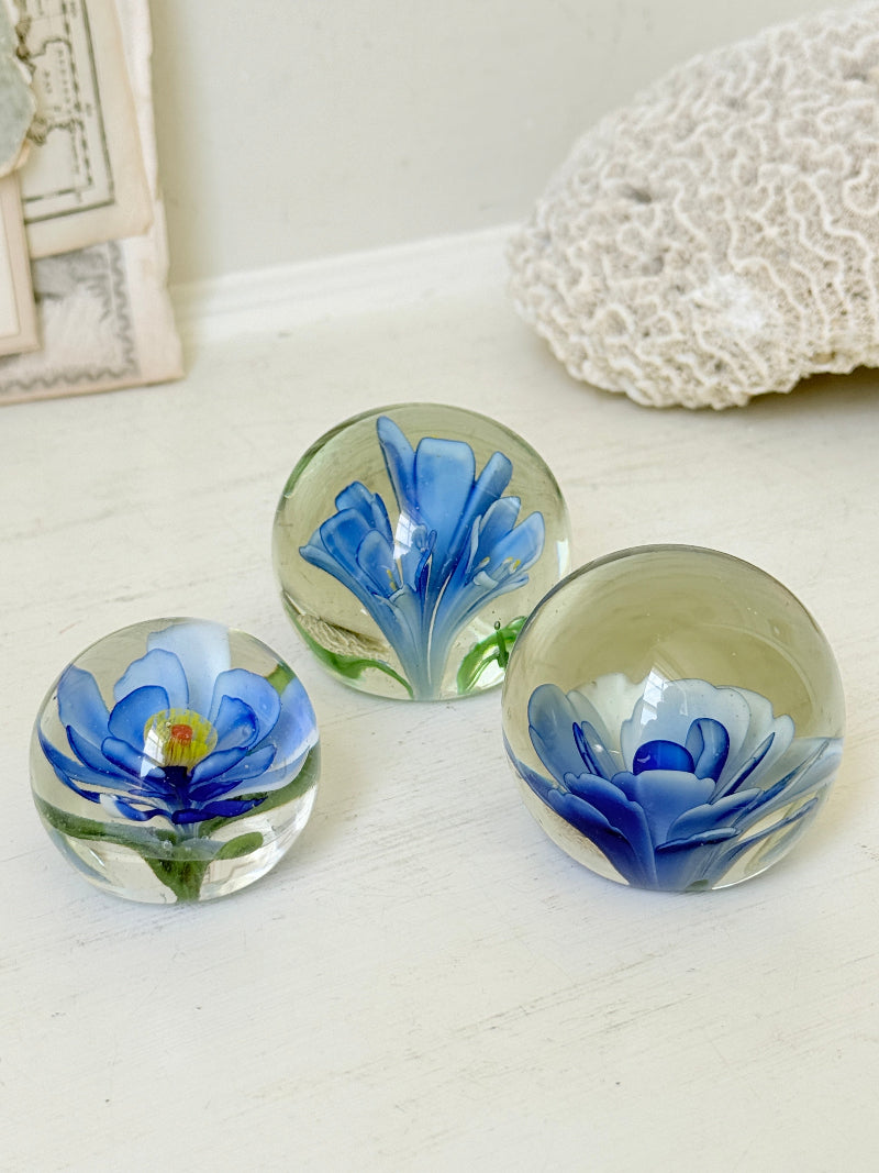 Trio of vintage glass paperweights with hand worked blue floral detail, clear glass domes and green leaf decoration