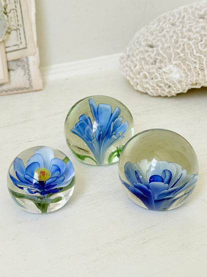 Trio of vintage glass paperweights with hand worked blue floral detail, clear glass domes and green leaf decoration