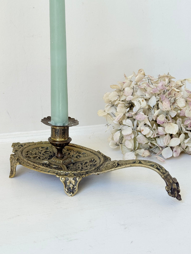 Ornate vintage brass candlestick with decorative handle and footed base, photographed on a white surface