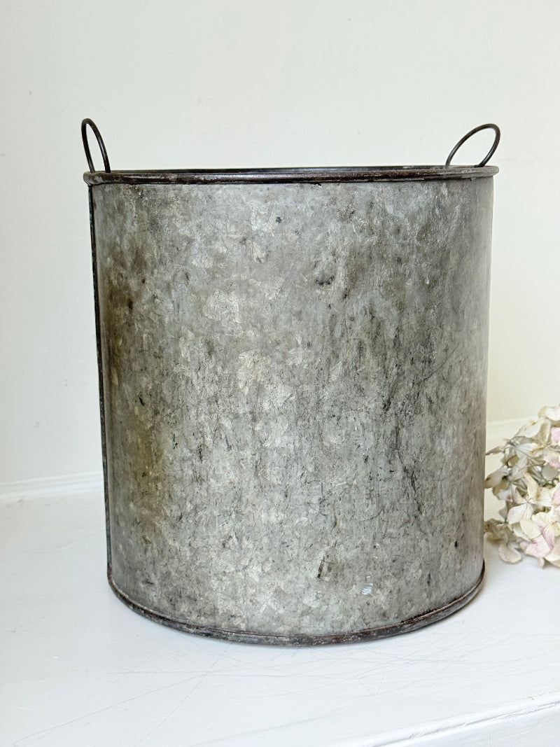 Vintage galvanised metal bin with handles, photographed on a white surface.