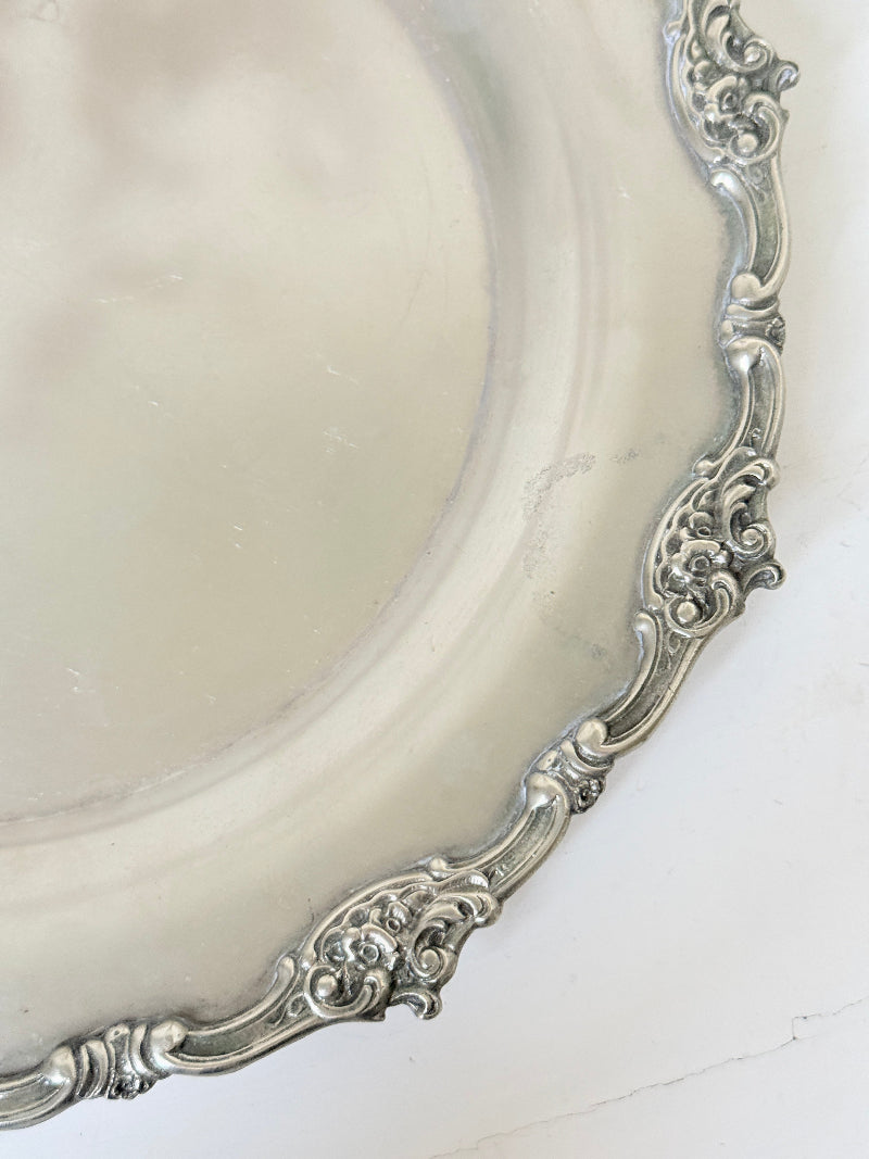 Vintage silvertone metal tray with ornate border, photographed on a white surface