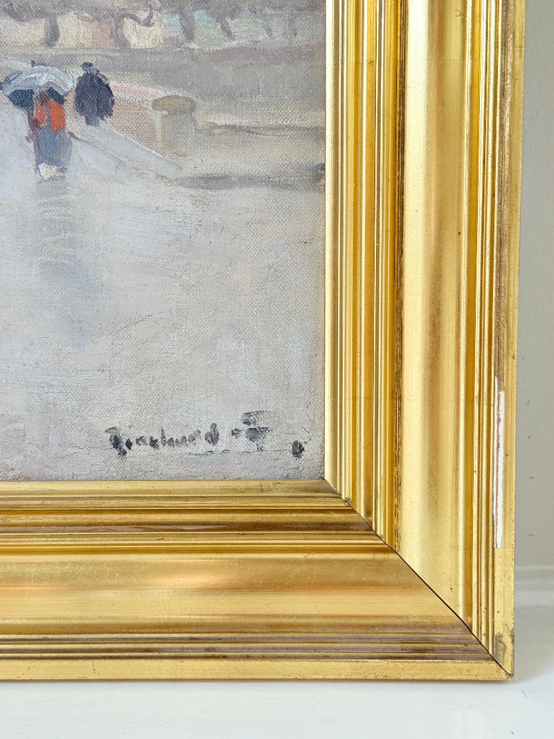 Close-up of a framed painting showing part of a snowy street scene with two figures carrying umbrellas, rendered in muted gray, white, and blue tones, with a prominent gold frame.
