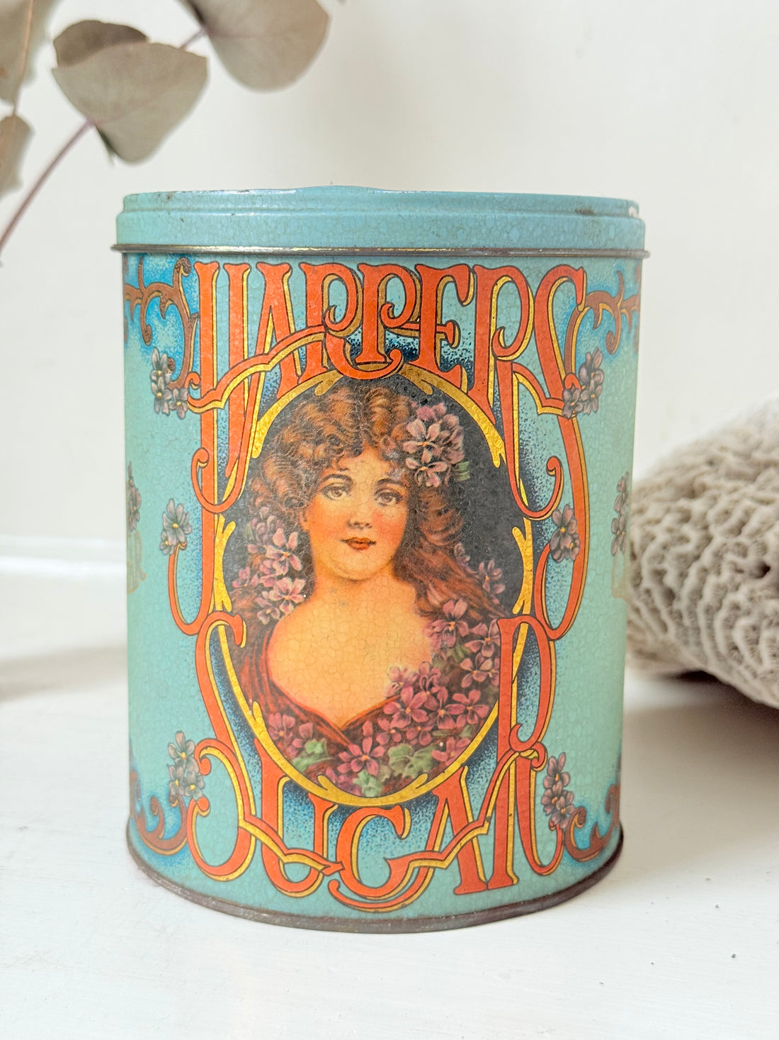 Vintage turquoise and gold metal sweet tin with Art Nouveau woman portrait photographed on a white surface.