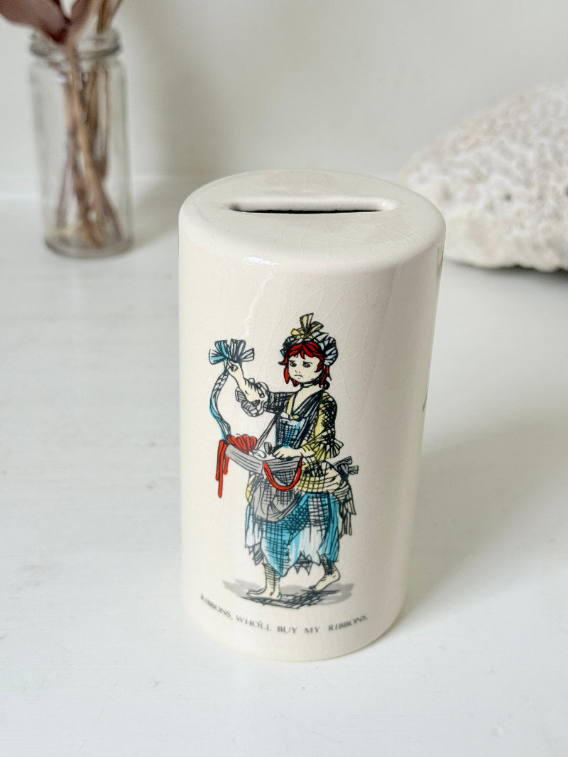Vintage ceramic money box with illustrated figures photographed on a white surface