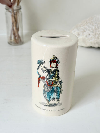 Vintage ceramic money box with illustrated figures photographed on a white surface