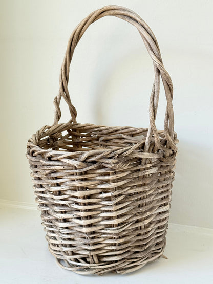 Rustic vintage wicker basket with woven handle and aged natural finish photographed on a white surface