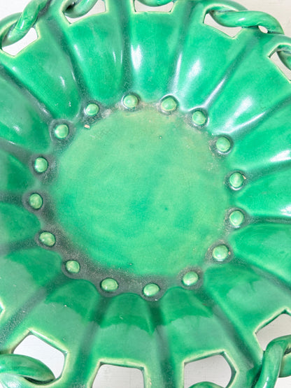 Close-up of a glossy green ceramic plate with a scalloped rim, raised circular details, and cutout sections near the edge.