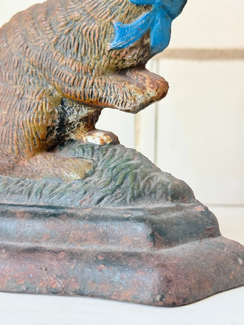 Close-up of a decorative cast-iron dog statue with a textured brown and gray body, a blue bow on its head, and a tiered base.