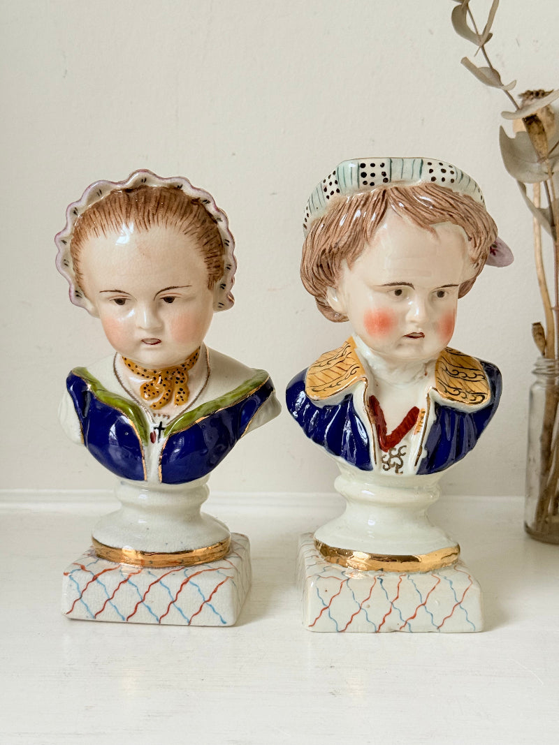 Hand painted Victorian Staffordshire ceramic children busts on white surface, photographed beside dried stems.