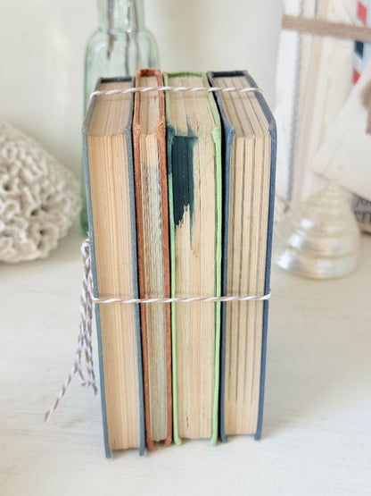 A stack of four vintage hardcover books tied together with white string, standing upright on a light surface with a softly blurred background.