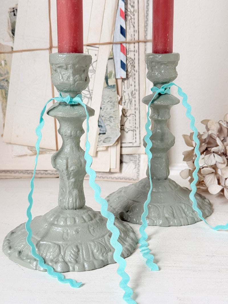 Two ornate gray candlestick holders with red taper candles tied with light blue ribbon, set against a vintage-style collage background.