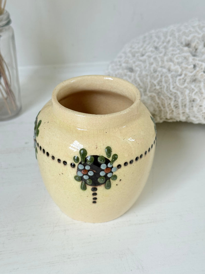 Cream studio pottery decorative pot with raised green floral motif, photographed on a white surface