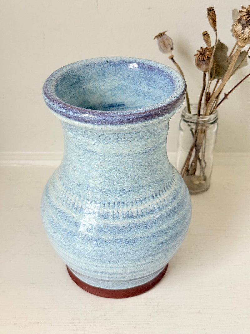 Studio pottery vase with sky blue glaze, indigo rim, and natural red clay base, photographed on a white surface