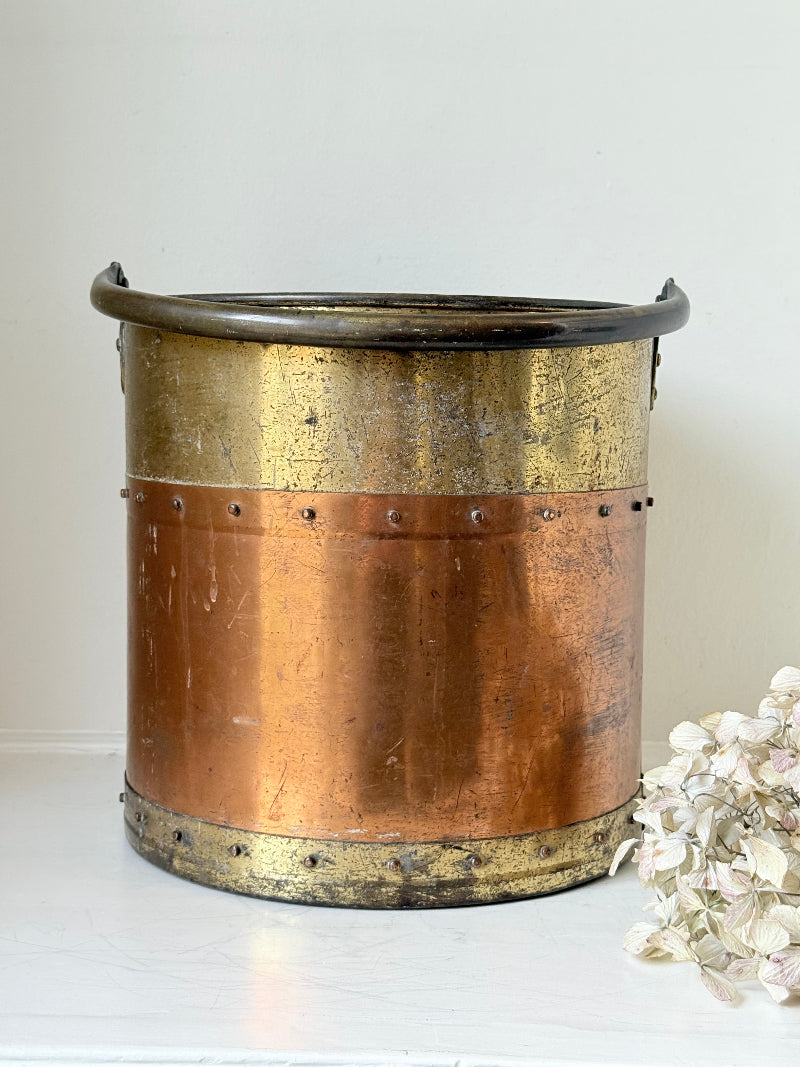 Vintage copper and brass metal bin with handle, photographed on a white surface.