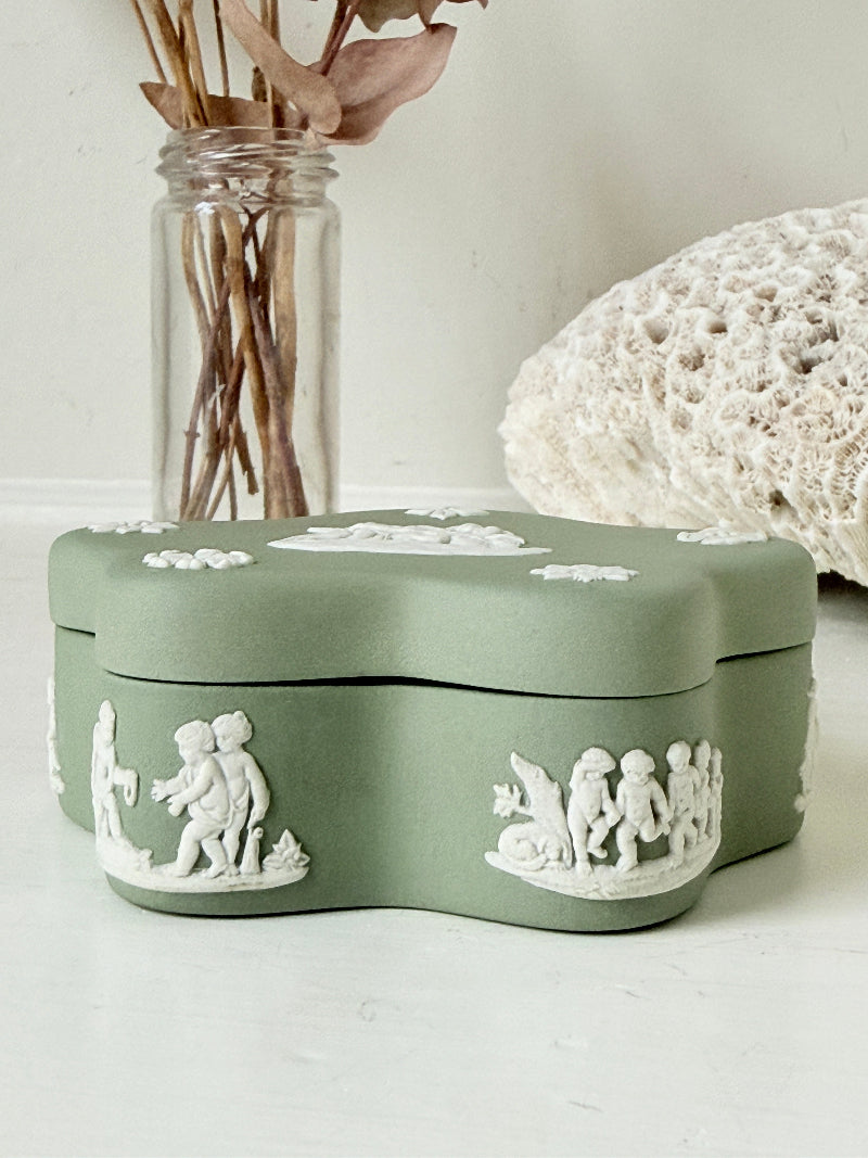 Vintage Wedgwood Jasperware sage green lidded trinket box in a quatrefoil shape, decorated with white neoclassical cherubs and florets, styled with dried stems.