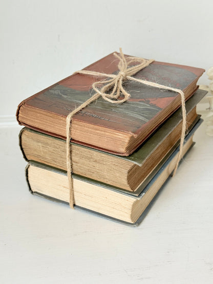 Vintage decorative book bundle in red, olive green and cream tied with twine, photographed on a white surface