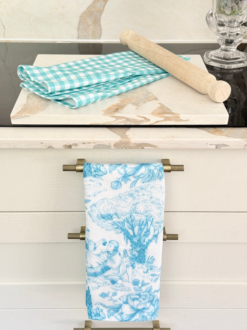 Turquoise gingham check cotton tea towel draped over a white plate on a marble surface with an orchid behind