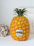 A novelty container shaped like a pineapple, with a textured golden-yellow body, green leafy crown, and a silver label reading &