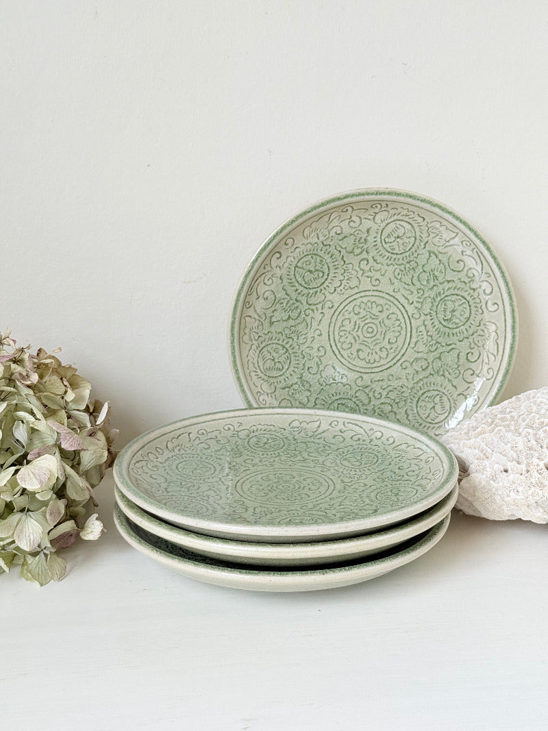 Set of four Thai stoneware plates with soft green celadon glaze on white surface