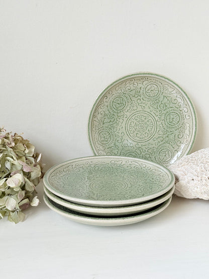 Set of four Thai stoneware plates with soft green celadon glaze on white surface