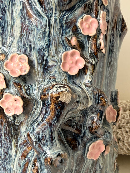 Large ceramic tree trunk vase with applied pink cherry blossom detail, textured bark form and dark drip glaze