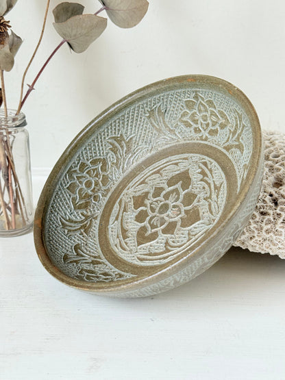 Studio pottery bowl with carved floral and geometric decoration in neutral glaze, photographed on a white surface with a pear inside.