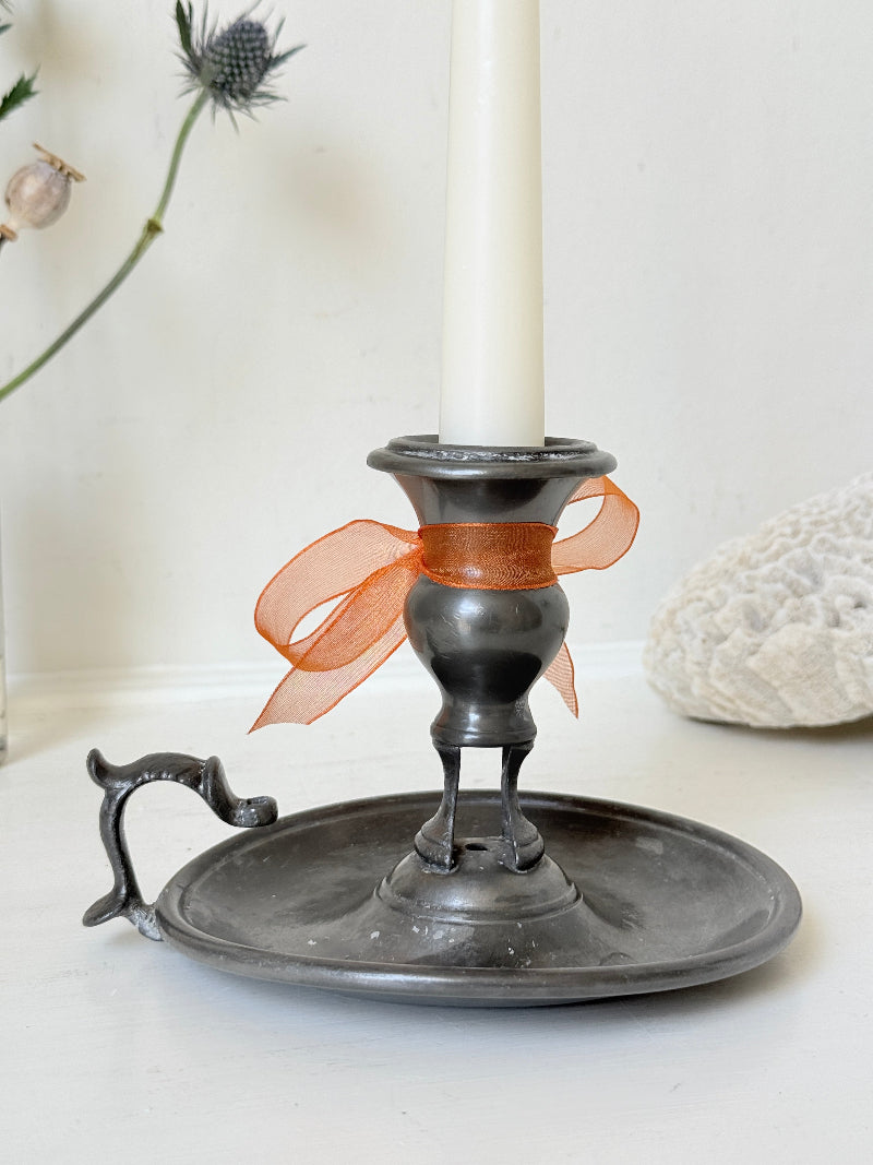 Vintage pewter chamberstick with handle and circular tray, photographed on a white surface