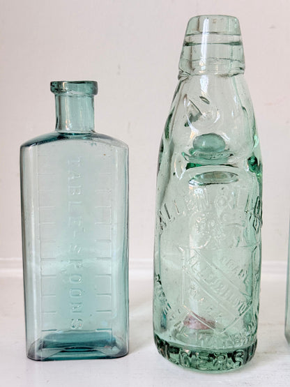 Set of five antique aqua green glass bottles with embossed lettering, photographed on a white surface