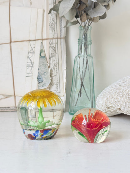 Pair of yellow and red flower glass paperweights with green stems, photographed on a white surface