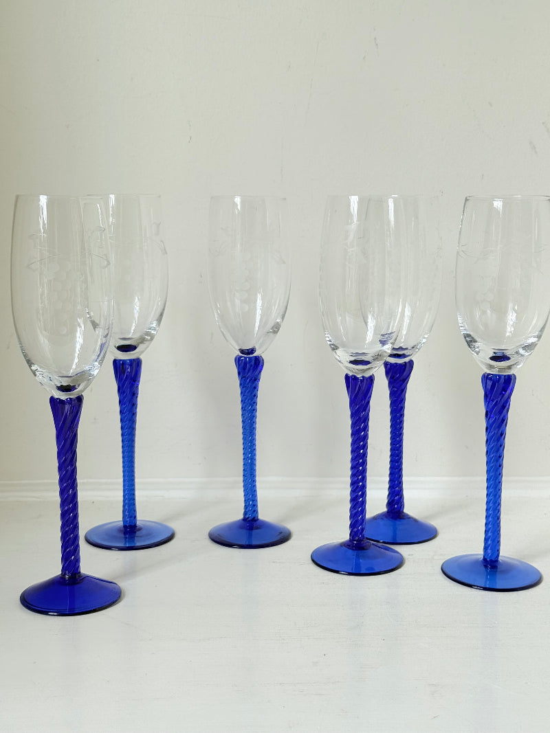 Set of six vintage French champagne flutes with tall clear bowls and cobalt blue twisted stems, photographed on white surface.