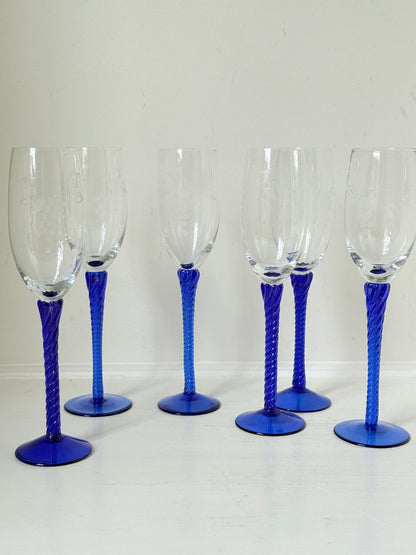 Set of six vintage French champagne flutes with tall clear bowls and cobalt blue twisted stems, photographed on white surface.