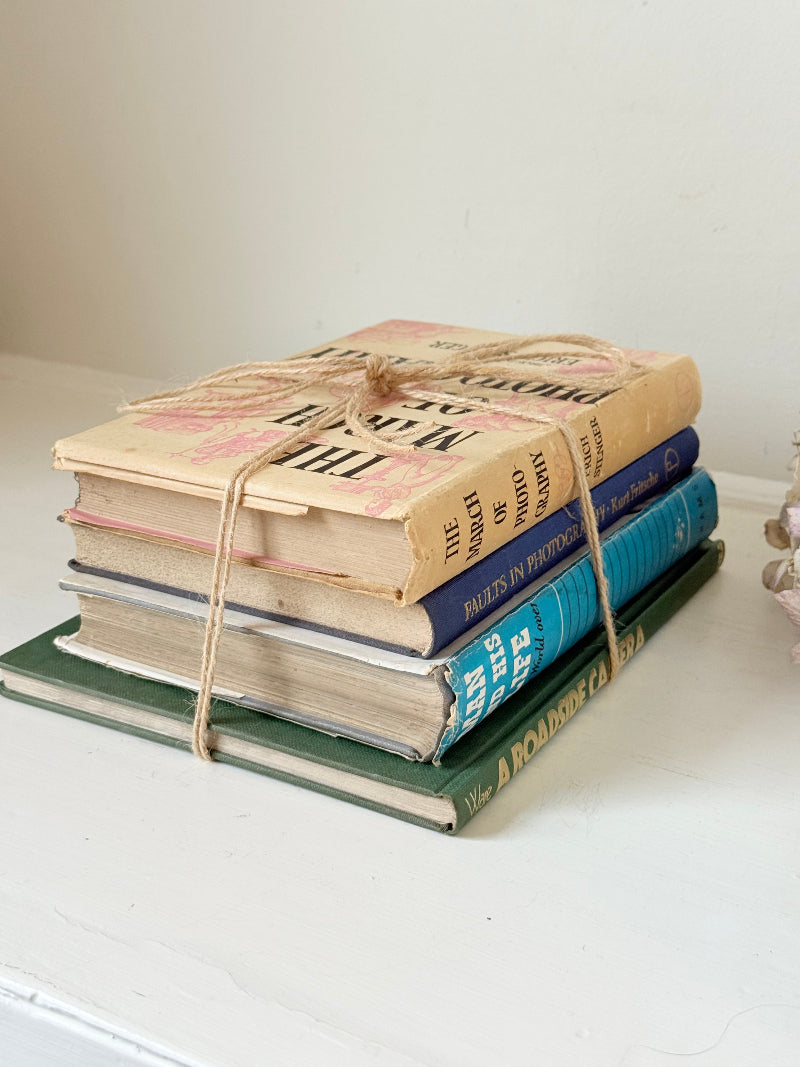 Bundle of vintage books in blue and neutral tones tied with twine, photographed on a white surface
