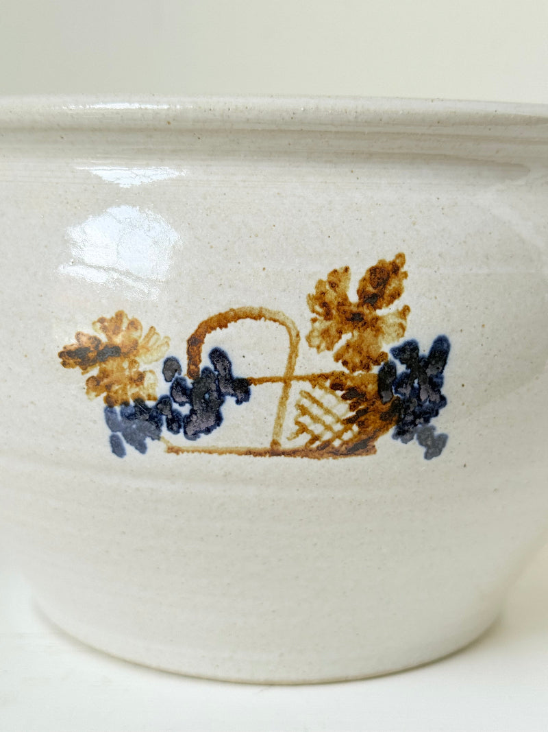 Large studio pottery bowl with hand-painted grape motif and side handles, photographed on a white surface