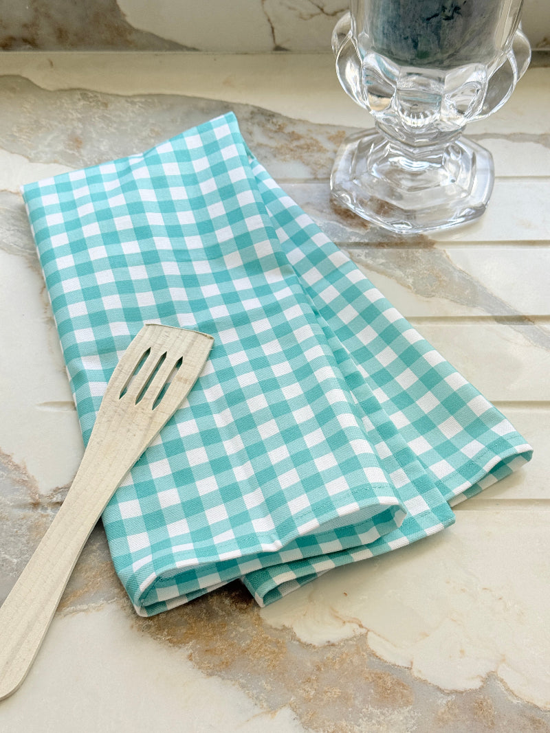 Turquoise gingham check cotton tea towel draped over a white plate on a marble surface with an orchid behind