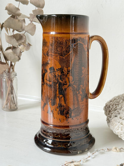 Antique Ridgways stoneware jug photographed on a white surface in amber treacle glaze with A Christmas Visitor black transfer scene and tall handle