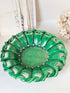 A green ceramic decorative bowl with a wavy, scalloped rim and cutout details, displayed on a white surface with neutral background decor.