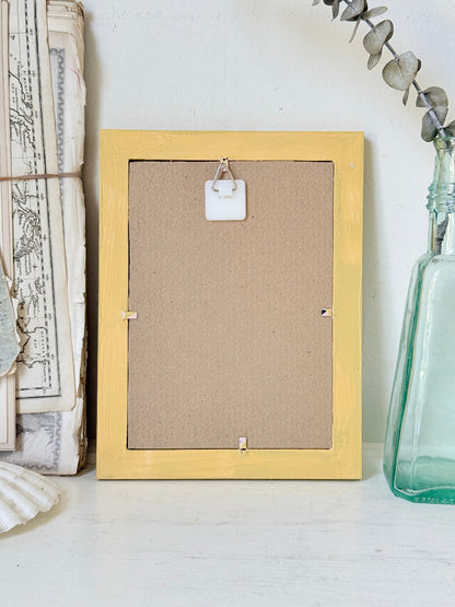 Framed Victorian cookery illustration of a celebration cake from 1896 in a mustard yellow frame displayed on a white surface.