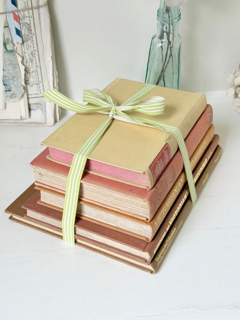 A stack of vintage hardcover books tied with a light green and white striped ribbon, set on a white surface with a soft, rustic background.