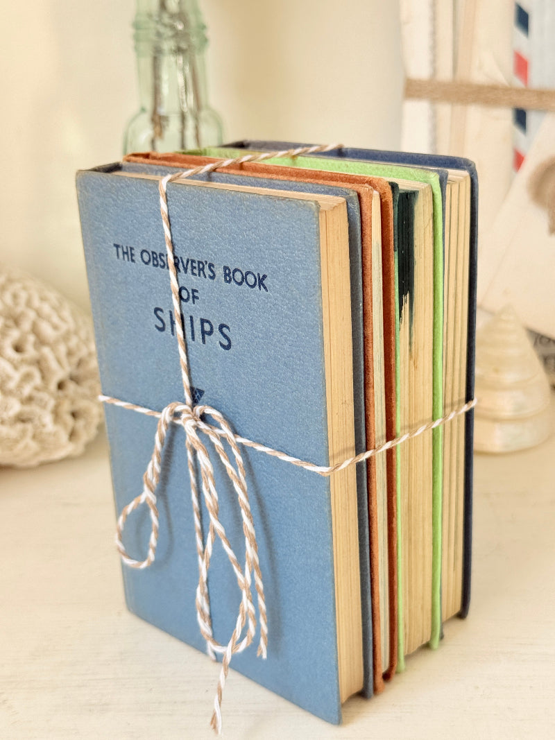 A stack of vintage-style hardcover books tied together with twine, featuring a prominent blue book in front with the text &