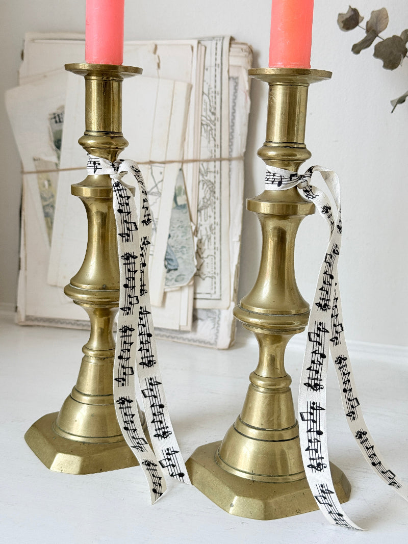 Pair of antique brass candlesticks with turned baluster stems and stepped bases holding coral tapers