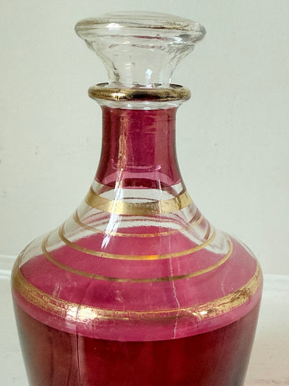 Vintage red printed glass cocktail set with clear glass decanter and six small glasses with gilt band rims, photographed on a white surface